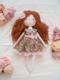Handmade rag doll wearing a green floral outfit with a decorative fabric rose hair clip